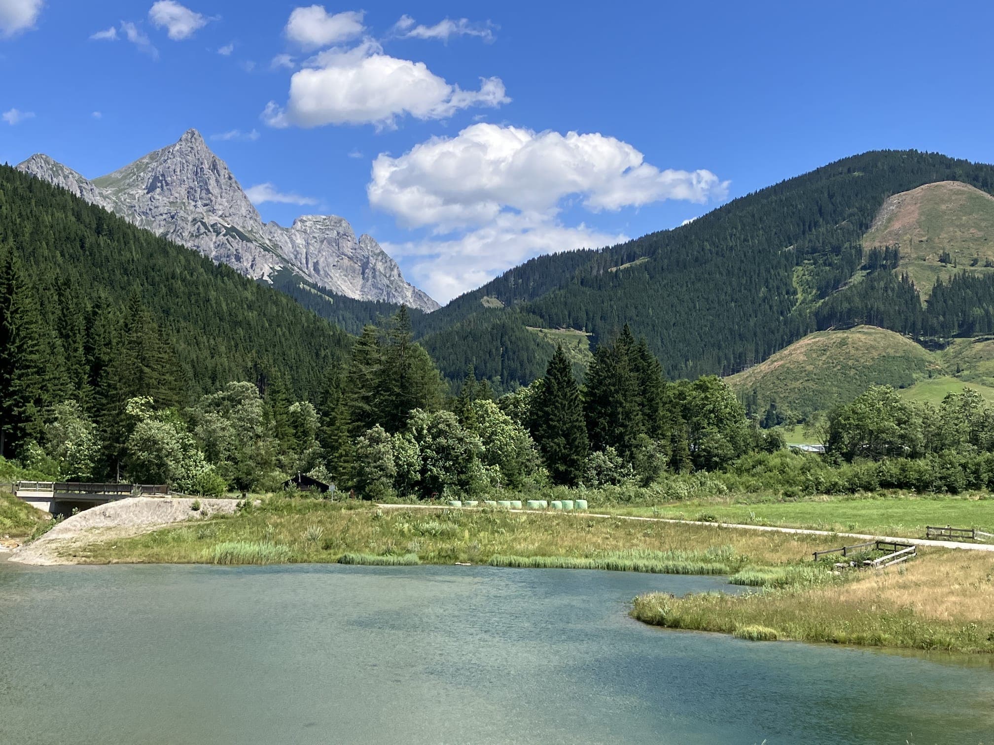 Klidná horská krajina – jezero, jehličnatý les a skalnatý vrchol pod modrou oblohou